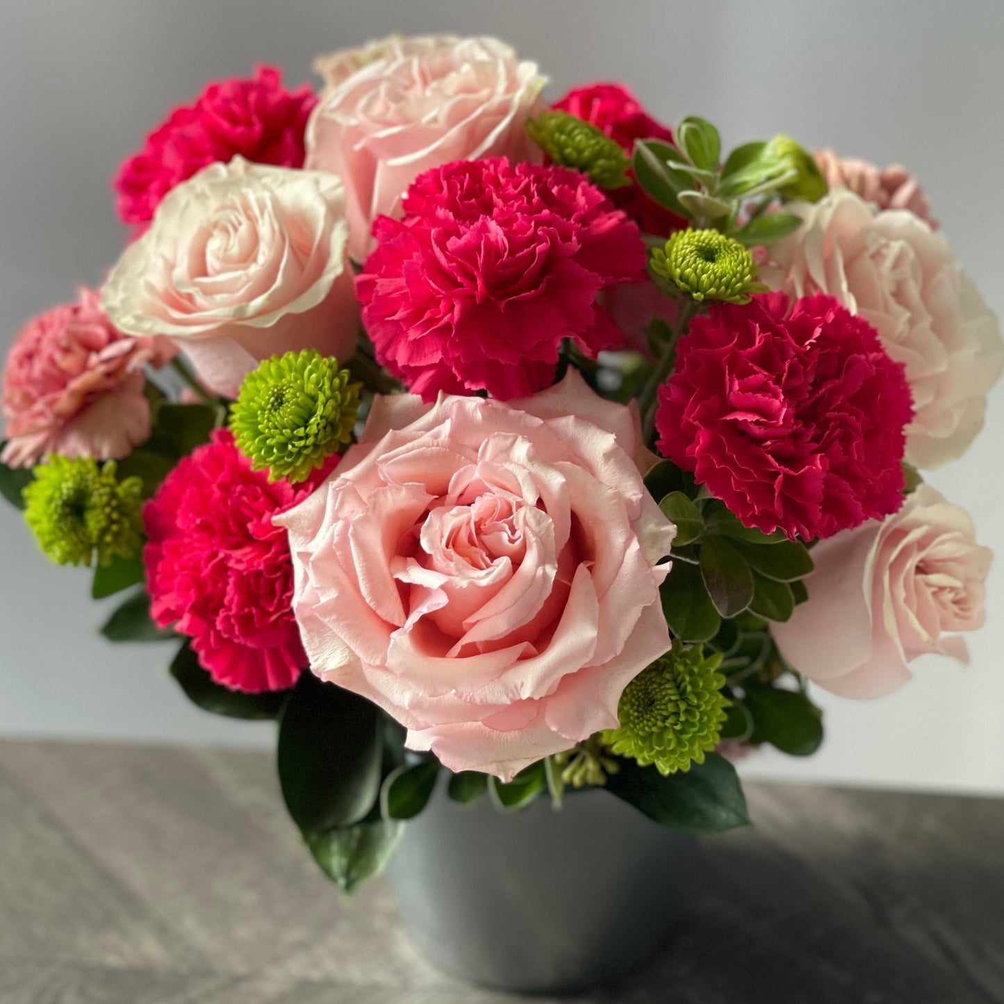 Light-pink roses, fragrant hot pink carnations, and fresh seasonal greenery with a touch of lawn-green button mums